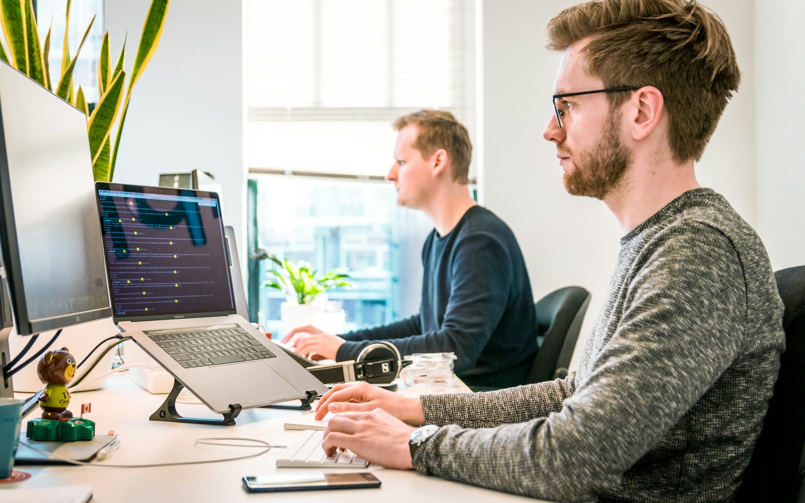 Two engineers reviewing code and monitoring output side by side at a workstation